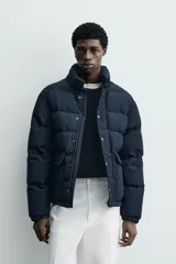 Campera puffer acolchada de corte regular fit, confeccionada en tejido técnico azul marino repelente al agua. Relleno interior de 80% plumón y 20% pluma. Cuenta con cuello subido, manga larga con puño elástico, bolsillos frontales de plastrón con solapa y cierre de cremallera oculta con solapa de botones a presión.
