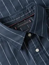 Camisa azul marino con diseño de rayas verticales blancas, de manga larga, corte amplio, cuello clásico y bolsillo de parche en el pecho con el logo bordado.
