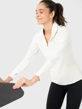 Buzo deportivo color crema de tela suave y delgada, con medio cierre frontal, cuello alto y mangas largas con orificios para los pulgares.