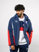 Campera de abrigo Umbro del Club Nacional de Football, con diseño de bloques de color en azul, blanco y rojo. Cuenta con capucha ajustable, cierre frontal y logo de la marca junto al escudo del club en el pecho.