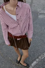 Camisa de manga larga con estampado de cuadros en tonos rosados y negros. Presenta cuello solapa, bolsillo delantero de plastrón, cierre frontal con botones y detalle de laterales ajustables con lazos.