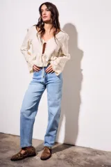 Blusa beige de viscosa y lino, con escote en V, mangas largas acampanadas con detalles bordados tipo broderie, y cierre frontal con lazo para anudar.