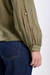Camisa casual manga larga color verde oliva, de tela traslúcida con textura sutil. Tiene cuello redondo, cierre frontal con botones y mangas largas con puños elásticos.