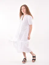 Vestido midi de broderie color blanco, con cuello mao y escote en V, cierre frontal con botones, mangas cortas abullonadas y detalle de volado en el ruedo.
