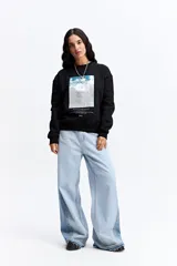 Buzo negro de algodón con cuello redondo, mangas largas y calce relajado. Presenta una estampa frontal rectangular con diseño abstracto en tonos celestes y blancos, acompañada de texto decorativo.