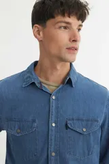 Camisa celeste de denim, corte regular fit, cuello solapa clásico, cierre frontal con botones a presión metálicos y dos bolsillos en el pecho con solapa.