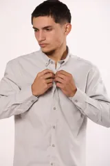 Camisa de manga larga en color gris, confeccionada en algodón, con cuello abotonado y cierre frontal de botones.