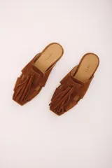 Zueco de cuero color marrón, estilo mule, con puntera cuadrada y tira ancha adornada con flecos. Suela plana.