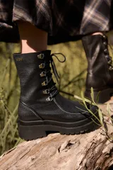 Borcego de caña corta confeccionado en cuero negro, con diseño de cordones y ganchos metálicos, cierre lateral y suela de plataforma dentada.