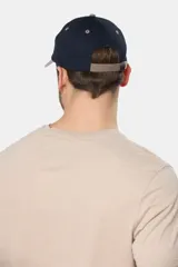 Gorro tipo gorra con visera de lona color azul, con parche tejido frontal que presenta diseño de paisaje y mar.