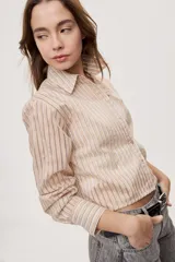 Camisa de manga larga con diseño de rayas verticales en tonos celestes, blancos y marrones, confeccionada en tejido semitransparente con cuello camisero y cierre frontal de botones.