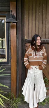 Sweater de hilo de algodón a rayas marrones y blancas, con cuello de cuero marrón y detalles bordados a mano en forma de cruz, acompañado de flecos colgantes en el pecho.
