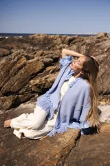 Ruana azul claro de edición limitada, tejida artesanalmente en lana merino con detalles de lino teñido a mano. Presenta flecos delicados y una combinación de texturas.