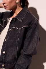 Campera de denim gris oscuro con tachas plateadas en cuello y solapas, corte cropped y mangas largas.