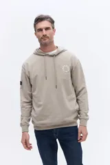 Canguro con capucha de algodón color beige, con cordones de ajuste y estampa circular frontal con el nombre de la marca y el año 1971.