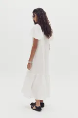 Vestido midi de lino color blanco, con cuello mao, cierre frontal con botones y mangas cortas con volados. Presenta un diseño holgado con un volado en el ruedo.