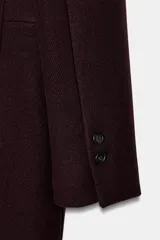 Abrigo largo de corte estructurado confeccionado en mezcla de lana, color bordó. Presenta cuello con solapa de muesca, cierre frontal con botones, mangas largas con detalle de botones en puños y bolsillos delanteros con solapa.