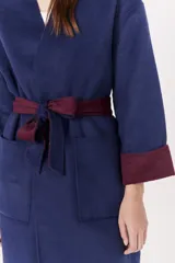 Tapado de paño azul marino con cuello solapa y mangas amplias. Presenta un cinturón de tela color bordó anudado a la cintura y puños doblados que dejan ver el forro bordó.