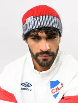 Gorro tipo beanie de punto acanalado en color azul marino, con vuelta en color rojo y blanco a rayas. Incluye etiqueta lateral con el logo de Umbro y el escudo del Club Nacional de Football.