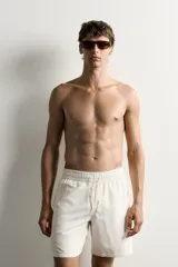 Short de baño largo en color beige, confeccionado en tejido técnico con tacto aterciopelado. Cuenta con cintura elástica ajustable con cordón, bolsillos laterales y detalle de bolsillo trasero, además de forro interior.