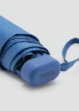 Paraguas mini plegable de color azul, con diseño liso y correa de mano a juego. Incluye detalle de placa metálica con logo de la marca.