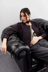 Campera bomber corta a la cintura con cuello redondo, confeccionada en jacquard con estampado de leopardo en tonos morados y marrones. Presenta una cartera frontal con cierre adornada con piedras y strass.