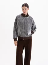 Campera tipo bomber con cierre frontal, cuello alto, puños y ruedo en tejido acanalado color marrón. Presenta un diseño estampado con patrón de espiga en tonos blanco y negro.