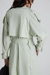 Trench color verde claro con cuello solapa, doble botonadura, cinturón y bolsillos laterales.