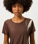 Remera deportiva de mujer Get Over, confeccionada en microfibra blanca con cuello redondo, manga corta y un diseño estampado de ondas en color verde y marrón en el lateral izquierdo.