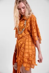 Vestido camisero oversize de color naranja en tela calada con diseño geométrico, cuello tipo solapa, mangas anchas y ruedo con terminación en picos. Cuenta con lazo ajustable en la cintura.