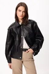 Chaqueta de cuero sintético negro con textura granulada, corte oversize, cuello camisero, cierre frontal con botones a presión, bolsillos frontales con solapa y charreteras en los hombros.