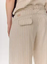Pantalón sastrero de corte ancho, color beige con rayas verticales blancas y detalles de costuras pespunteadas.