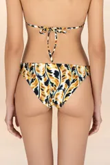 Calzón de bikini de corte a la cadera con cobertura pequeña. Presenta un estampado abstracto en tonos mostaza, negro y blanco, con un diseño que simula hojas o manchas. Es reversible, ofreciendo un segundo look.