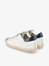 Zapatillas urbanas Golden Goose modelo Super-Star, de cuero blanco con efecto desgastado, estrella lateral en cuero perforado, puntera en gamuza gris, talón en cuero azul marino y cordones grises.