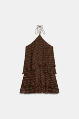 Vestido mini de cuello halter con diseño de volantes escalonados. Presenta estampado de lunares, cierre lateral con cremallera oculta y lazada ajustable en el cuello.