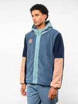 Campera de polar con capucha, cierre frontal completo y diseño en bloques de color azul y azul marino. Presenta detalles en nylon en la zona del cierre y la capucha, con logo de la marca aplicado en el pecho.