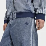 Jeans de mezclilla Adidas de pierna recta, efecto acid wash, con corte holgado, tiro medio y las clásicas tres tiras laterales. Cuenta con bordado del trébol de la marca.