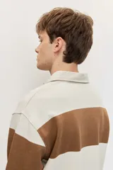Chomba de friza de manga larga con diseño de rayas horizontales anchas en color beige y azul, cuello polo y pequeño bordado en el pecho.