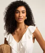 Enterito corto blanco sin mangas confeccionado en viscolino con escote V, espalda descotada con volados en el escote. Posee cinturón con hebilla redonda de ráfia y trabillas en la cintura.