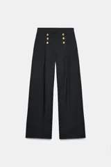 Pantalón de tiro alto con pierna ancha, confeccionado en sarga color tostado. Presenta detalle de doble hilera de botones metálicos dorados en el frente y pinzas verticales.