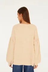 Cardigan largo de punto texturizado color beige, con escote en V, mangas largas voluminosas y cierre frontal con botones dorados con relieve.