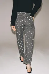 Jeans de tiro medio con corte relajado y largo al tobillo. Presenta un diseño de cinco bolsillos, cierre frontal con cremallera y botón metálico, y un estampado integral de lunares blancos sobre fondo gris oscuro.