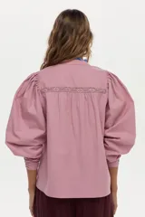 Blusa de algodón liviano color blanco, con detalles de puntilla en el frente, cuello mao con escote en V, cordón colgante y mangas largas abullonadas con puños ajustados.