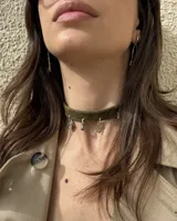 Gargantilla tipo choker de gamuza color verde oliva, con dijes colgantes artesanales de metal y perla natural. Diseño ajustable con tiras para atar en la parte posterior.