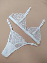 Conjunto de lencería de encaje blanco, compuesto por un soutiene de diseño triangular y una bombacha tipo colaless regulable.