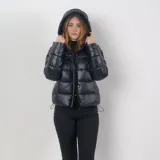 Campera puffer negra, acolchada y liviana, con capucha, cuello alto, cierre frontal con cremallera y botones a presión, dos bolsillos externos y sistema de ajuste regulable en la parte baja.
