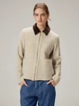 Chaqueta de lana hervida en color beige, con cierre frontal metálico y cuello camisero en contraste de color marrón oscuro. Presenta bolsillos frontales tipo parche y paneles laterales con textura diferenciada.