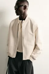 Campera bomber color verde militar de corte relaxed fit, confeccionada en tejido efecto ante, con cuello, puños y dobladillo en rib elástico, bolsillos frontales de vivo y cierre central con cremallera.
