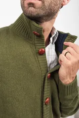 Cardigan de punto color verde oliva, con cuello alto, cierre frontal de botones grandes en tono marrón y bolsillos frontales tipo parche.