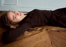 Vestido midi marrón oscuro de corte recto y escote en V, con mangas largas y un cinturón fino con hebilla metálica dorada en la cintura.